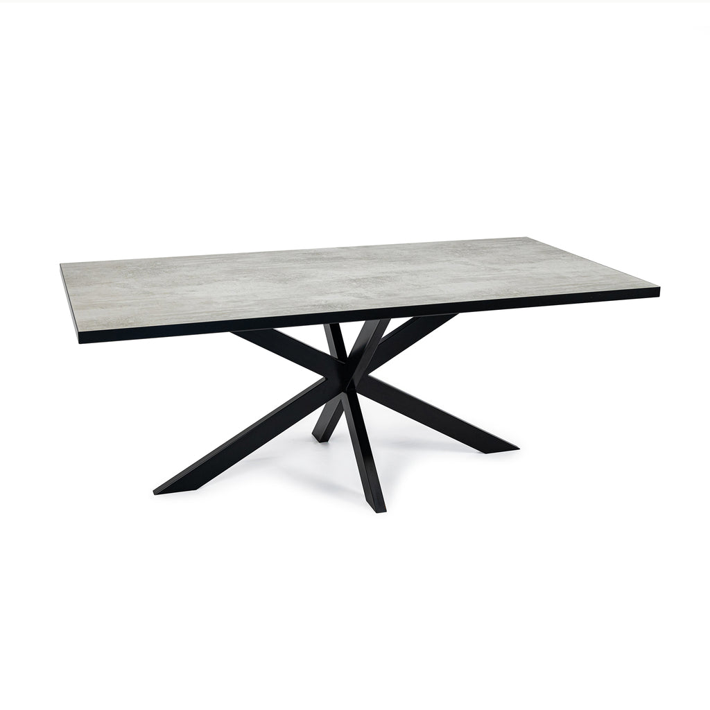 Strakke rechthoekige tafel met betonnen blad en zwarte, geometrische pootstructuur op witte achtergrond.
